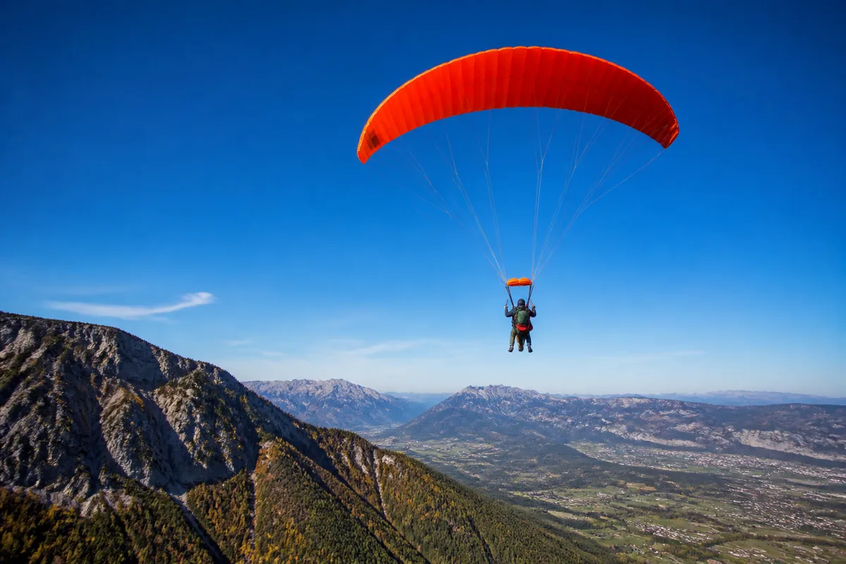 Parachutiste en tandem sous voile ouverte au-dessus d&rsquo;un relief montagneux
