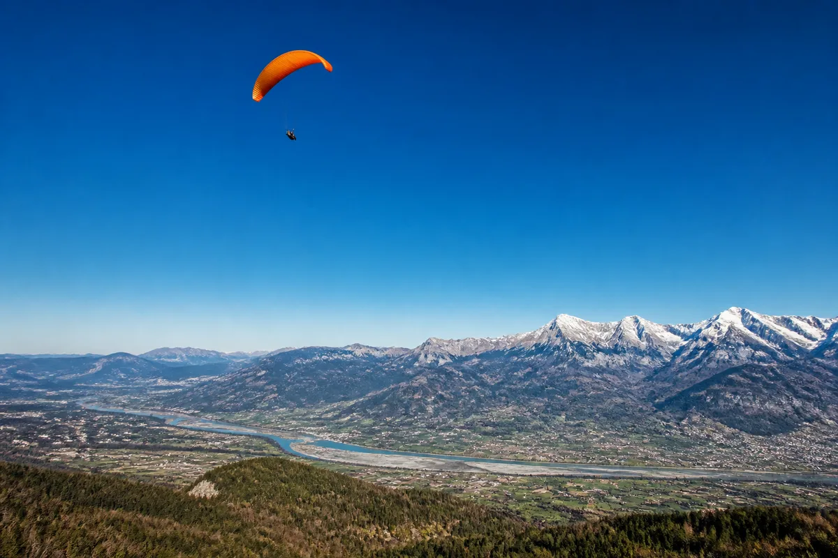 Voile de parachute colorée déployée au-dessus d’une vallée alpine sous un ciel bleu dégagé